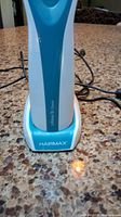 Front view of HairMax LaserComb in its blue and white charging stand on a countertop.