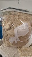 Tan fabric comforter set packaged in clear plastic with visible reversible comforter sides and included items.