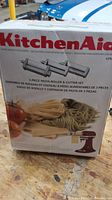 Box of KitchenAid 3-piece pasta roller and cutter set with images of pasta types and mixing bowl attachment compatibility.