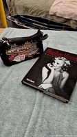 Photo showing clutch purse with Las Vegas design and Marilyn Monroe book side by side on a blue textured fabric surface