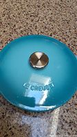 Top view of the turquoise lid with metal knob and embossed LE CREUSET.