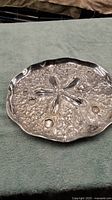Front view of shiny metal serving tray with raised sand dollar design and textured surface.