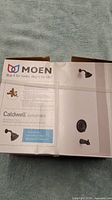 Front of the box showing the Moen branding, model Caldwell 82496EPBRB, and an image of the faucet set in Mediterranean Bronze.