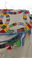 Close-up photo showing folded vintage queen size patchwork quilt with multicolor curved pattern and blue border.
