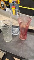 Set of three glass vases on dark surface showing clear and pink ribbed design vases with different shapes and sizes.