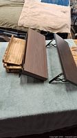 Multiple wooden shelf boards stacked, showing dark brown and natural wood finishes, placed on a cloth surface.