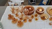Full set of various amber glass plates, glasses, and candle holders displayed on white cloth.