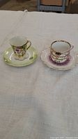 Two vintage porcelain teacups placed on matching saucers, showing front decorative sides.