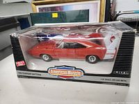 Front view of the model car inside its packaging showing the red 1969 Dodge Charger Daytona with American Muscle branding.