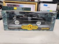 Front view of the 1949 Mercury Coupe diecast model and its packaging showing the car in black with whitewall tires and American Muscle branding.