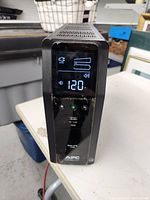 Front view of APC Back-UPS 1500 showing digital display with input voltage reading and power buttons with USB ports.