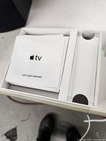 Original white Apple TV box with user manual and packaging inserts inside.