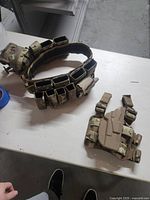 Two camouflage army utility belts laid on white surface, one multi-magazine pouch belt and one leg holster belt.