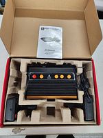 Atari Flashback 5 console and two joysticks in molded cardboard tray with user manual on top inside open box.