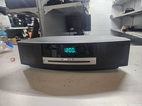 Front view of black Bose Wave Music System powered on displaying 12:00, showing front CD slot and speakers.