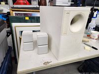 View of the Bose subwoofer and two smaller satellite speakers on a table, showing size and condition.