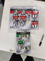 Photo showing Saturn Collection keyed entry door knobs and deadbolt keyed locks in unopened packaging, stainless steel finish with red label tags