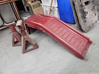 Image showing two red metal car ramps and two metal jack stands placed together on concrete floor.