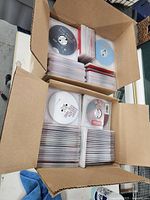Top view of two open cardboard boxes with many DVDs in plastic sleeves inside, some DVDs face up showing printed disc labels.