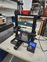Front angle of the Ender 3 Pro 3D printer on a table showing the printer's frame, print bed, and LCD control screen with knob.