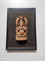 Front view of the framed wooden Ganesh carving showing the entire piece in a blue frame with black fabric background