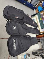 Three black guitar cases laid out side by side on the floor, identified as Gator, SX, and ChromaCast brands.