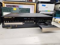 Front view of the Harman Kardon CD player showing the left disc tray extended and jammed, control buttons, and digital displays.