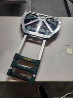 Folded hand truck showing green plastic handles with Harper label and silver metal base plate on table surface.