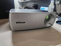 Front angle view of the silver InFocus projector on a table, showing the lens and casing.