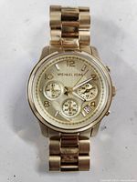 Front view of the Michael Kors gold-tone watch showing the dial, chronograph subdials, and date display.