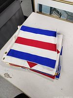 Folded set of multicolored nautical signal flags stacked on a table, showing blue and white stripes with red triangle design, and metal grommets on edges.