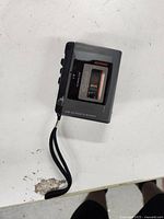 Angled view of the cassette recorder showing the side controls and wrist strap.