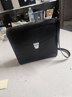 Black carrying case with strap and silver latch on white surface, store shelving in background