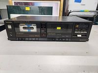 Front view of the Technics RS-T920 stereo double cassette deck showing two cassette compartments with tapes inside, power switch, play/rewind/stop controls, and various buttons and indicators.