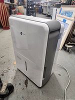 White Vremi dehumidifier upright on concrete floor in a warehouse-like setting.