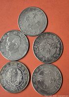 Five different silver one-dollar coins laid out on an orange surface