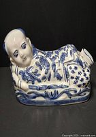 Front angle view of antique Chinese porcelain opium pillow shaped as reclining figure with detailed blue floral decoration.