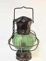 Front view of the antique kerosene lantern showing the green glass globe and metal wire cage.