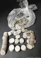 Clear plastic bag of loose and stacked silver quarters on a black background
