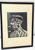 Framed black and white linocut print of a man in profile wearing glasses and a checkered shirt and hat.