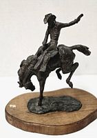 Front and left side view of bronze cowboy riding bucking bronco on wooden base.