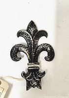 Front view of the 4 inch cast iron Fleur de Lis showing textured surface and black finish with white highlights.