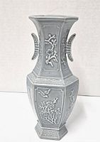 Front and side view of gray-blue celadon porcelain vase with relief floral and bird motifs, hexagonal shape, and wing-shaped handles.