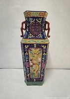 Front angle view of hexagonal cloisonne vase showing golden dragon and floral enamel designs on a cobalt blue background with red handles.