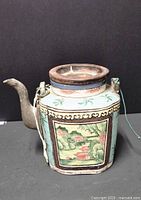 Front side view showing landscape scene with green trees, water, and buildings in multicolored enamel on stoneware teapot.