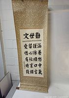 Full view of the large hanging Chinese calligraphy scroll showing gold patterned fabric, white calligraphy panel, and wooden rod at the bottom.