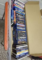 Box showing a large quantity of DVDs stacked vertically inside a cardboard box. Various genres and colors of cases visible.