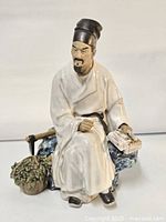 Front view of the seated scholar figurine showing detailed face, robe, and basket of flowers on side.