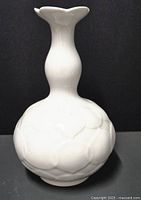 Front view of the white porcelain vase showing its rounded base and flared flower-shaped neck with embossed lotus flower pattern.