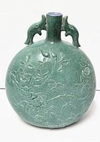 Front view of oval green glazed porcelain vase showing embossed floral motif and elephant head handles
